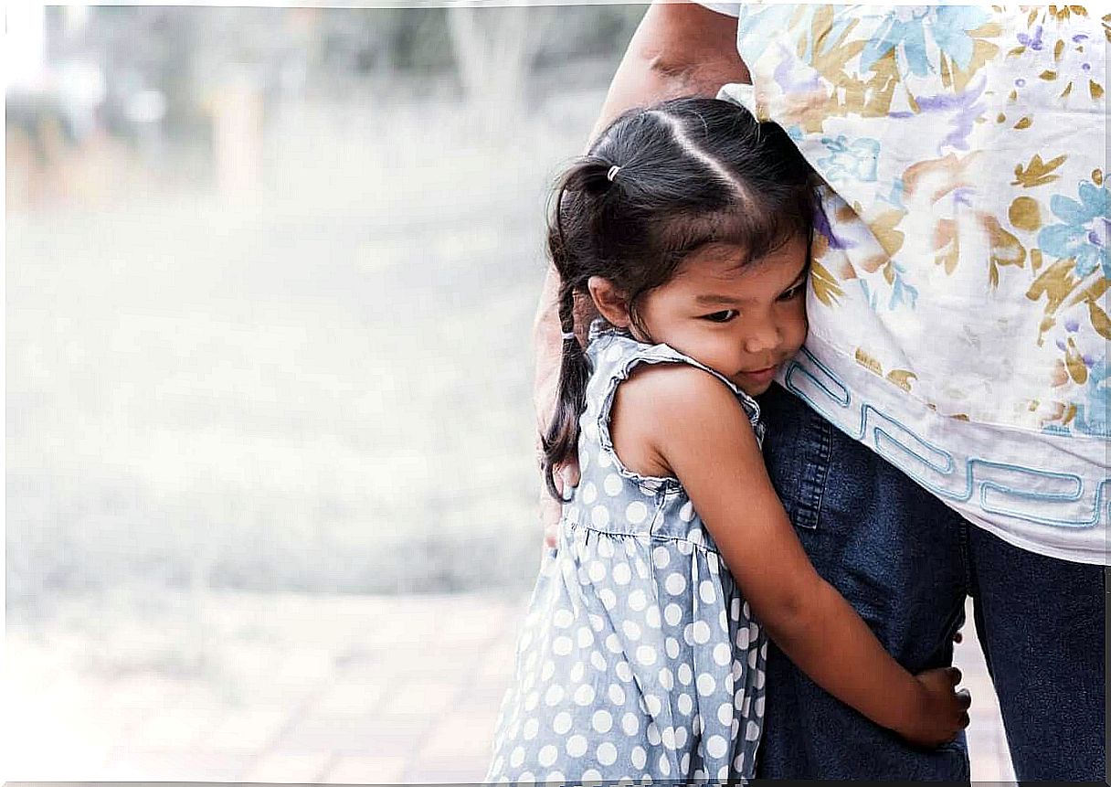 A young girl clings to her father's legs.