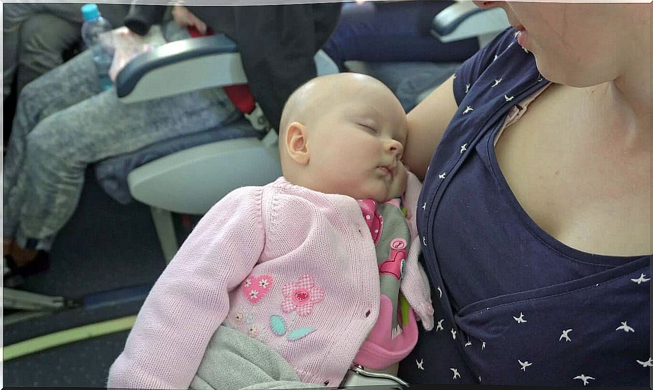 A mother holding her sleeping baby on a plane.