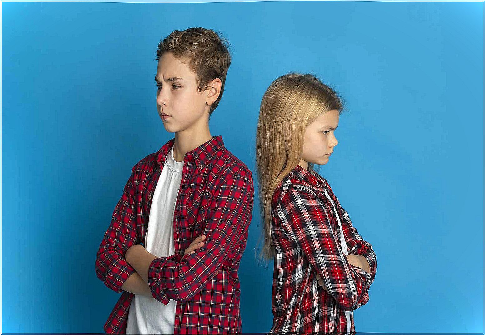 Two siblings with their backs to each other who look angry.