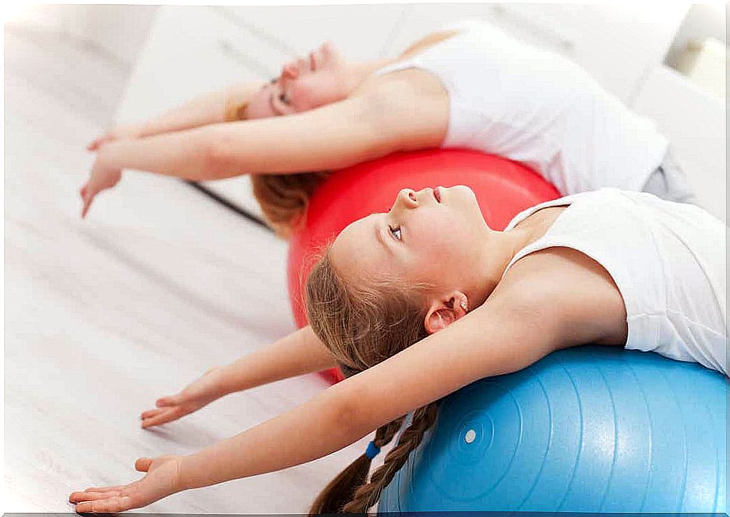 A mother and a daughter stretching over exercise balls.