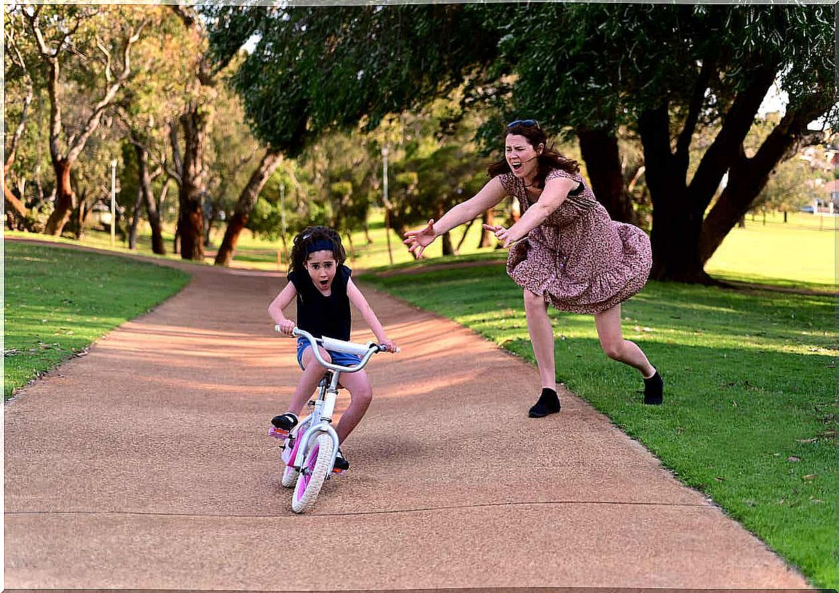 A mother runs to help her daughter who is losing balance on her bike.