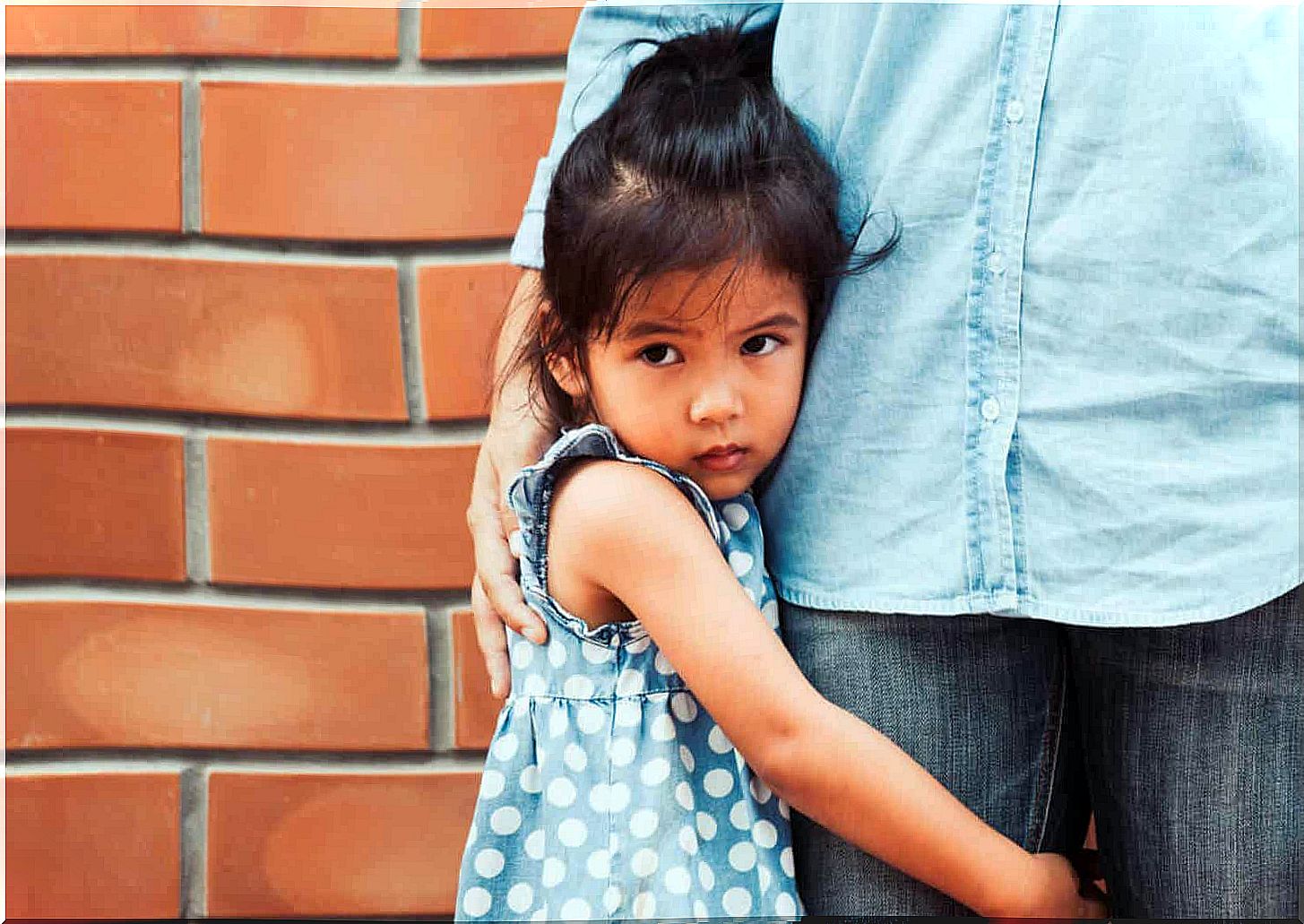 A small child hugging his parent's legs and looking scared.